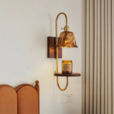 Sconce lit above a bed, a small jar resting on the walnut shelf