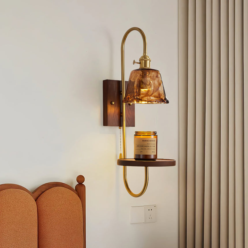 Sconce lit above a bed, a small jar resting on the walnut shelf