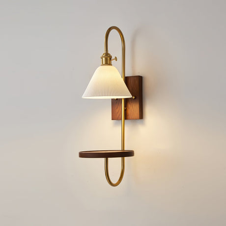 White shade lit on a brass hook arm above a walnut shelf on the wall
