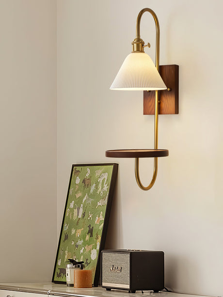 Sconce lit beside a leaning framed print with objects on the shelf