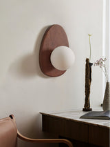 Sconce lit beside a dark console holding a vase of tall dried stems