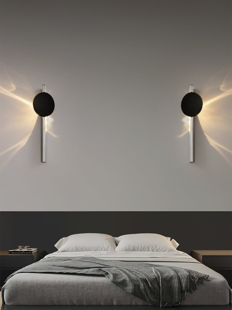 A pair of single disc lights glowing on each side of a bed with gray linens