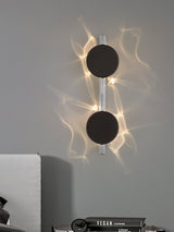 The two disc light lit on a gray wall above a bed with books on the nightstand