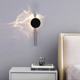 The single disc light lit above a white nightstand beside a cream headboard