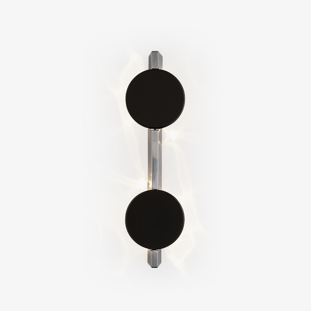 Wall light with two black discs on a polished rod, soft light rippling behind them