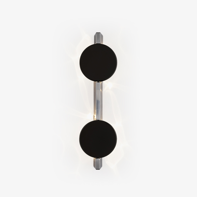 Wall light with two black discs on a polished rod, soft light rippling behind them
