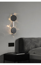 The two disc light above a black nightstand beside a gray headboard