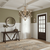 Lit above a dark console table with a round mirror on a green paneled wall