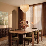 The fitting lit above a long dining table with chairs, curtains and flowers