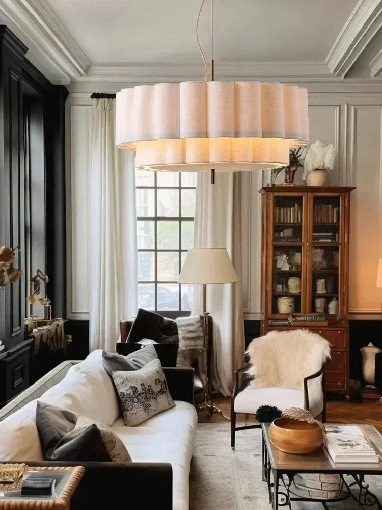 White drum pendant light lit in a dark paneled living room beside a tall window