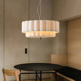 White drum pendant light hung over a round dining table in a wood paneled room