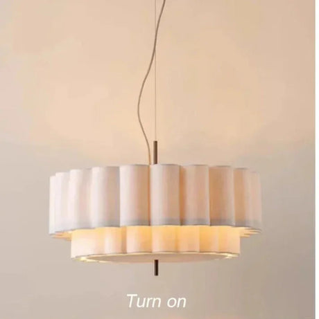 White drum pendant light switched on, warm glow escaping between the two scalloped tiers