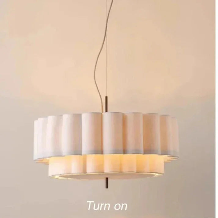 White drum pendant light switched on, warm glow escaping between the two scalloped tiers