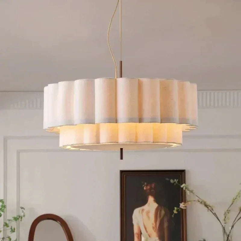 White drum pendant light with two scalloped fabric tiers lit above a paneled wall