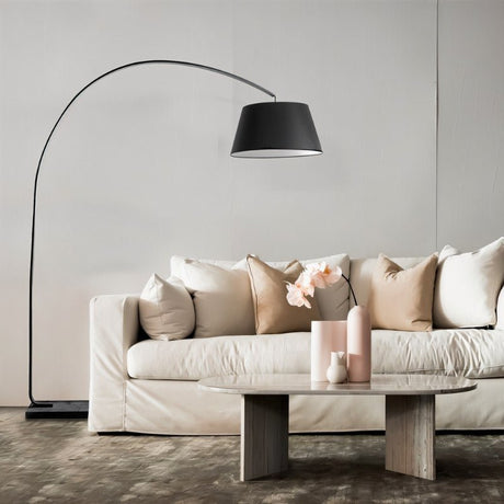 The lamp arching over a white sofa with cushions beside a pale round table