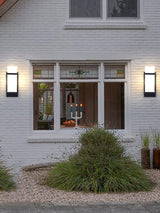 Two lights on a white brick house either side of a front window, ornamental grass below