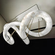 A long winding alabaster ribbon lit, held on brass cables from a slim frame