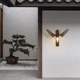 Sconce lit beside a doorway with a bonsai on a gravel bed beyond it