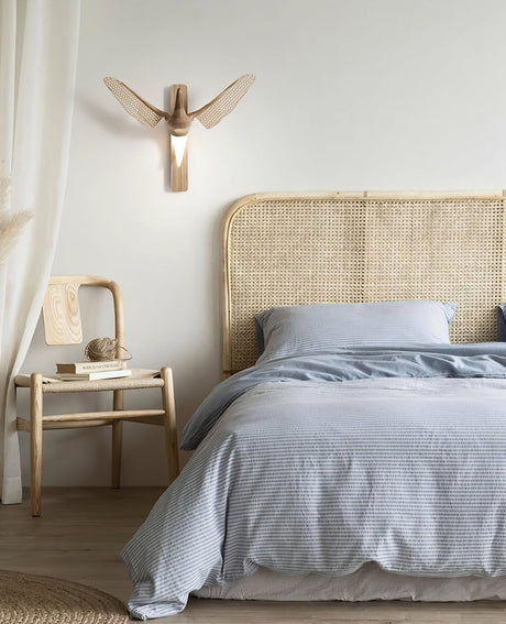 Sconce lit beside a cane headboard above a bed with pale linen