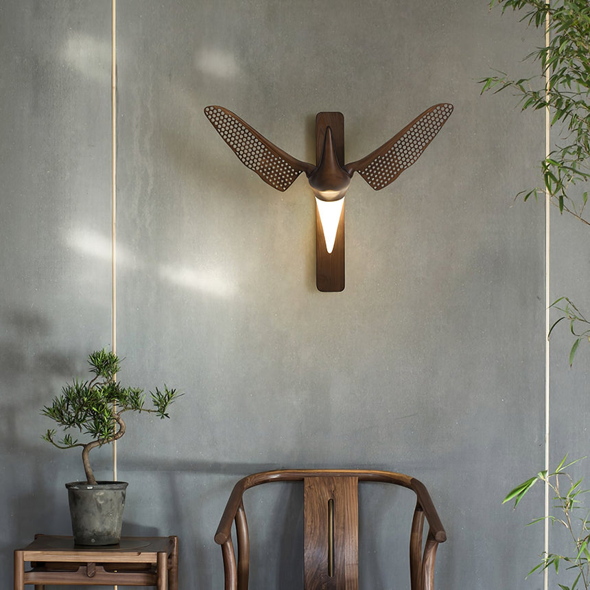 Sconce lit in a corner above a wood chair with a plant on a stool