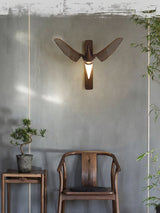 Sconce lit beside a wood chair and a side table with a small plant