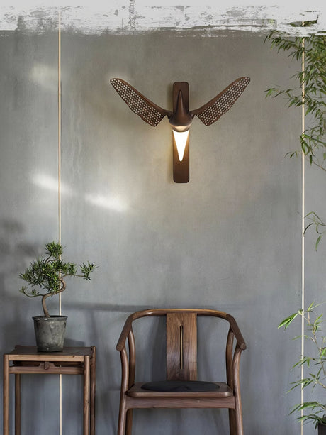 Sconce lit beside a wood chair and a side table with a small plant