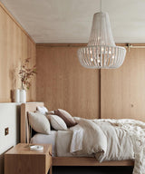 Hung over a bed against a pale timber wall with a nightstand and dried stems