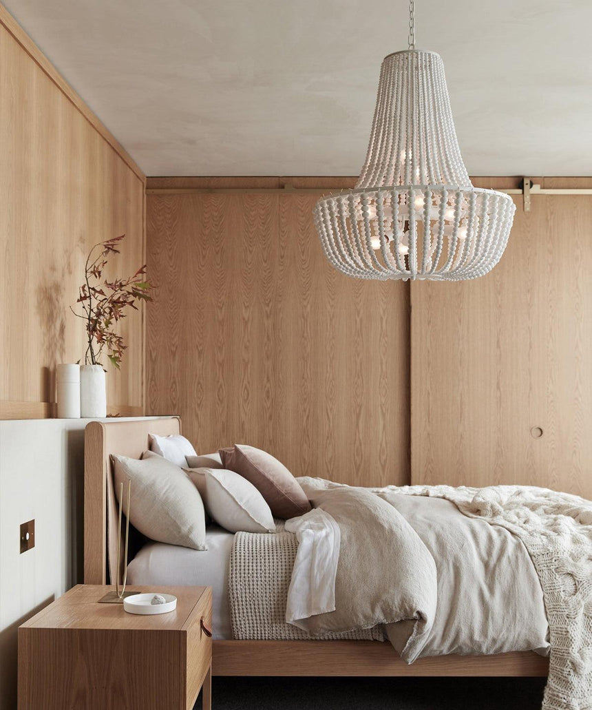 Hung over a bed against a pale timber wall with a nightstand and dried stems