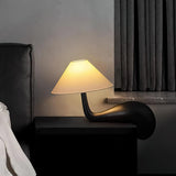 Dark wood desk lamp lit on a dark surface beside a curtain