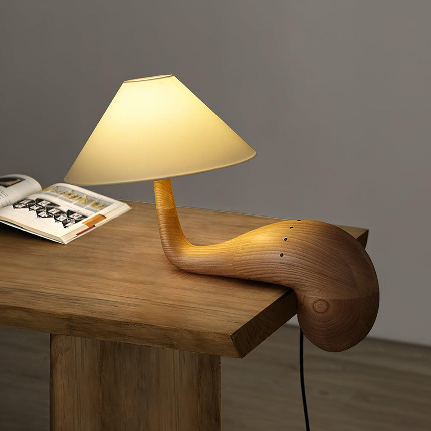 Wood desk lamp lit on a pale wooden desk beside a paint palette