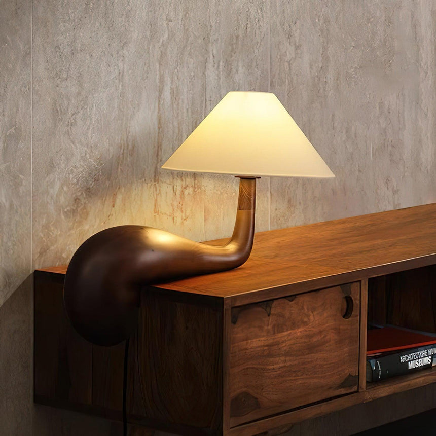 Wood desk lamp lit on a wooden media unit against a plaster wall