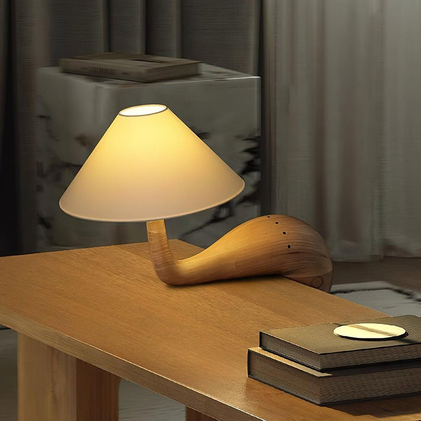 Wood desk lamp lit on a wooden desk beside a stack of books