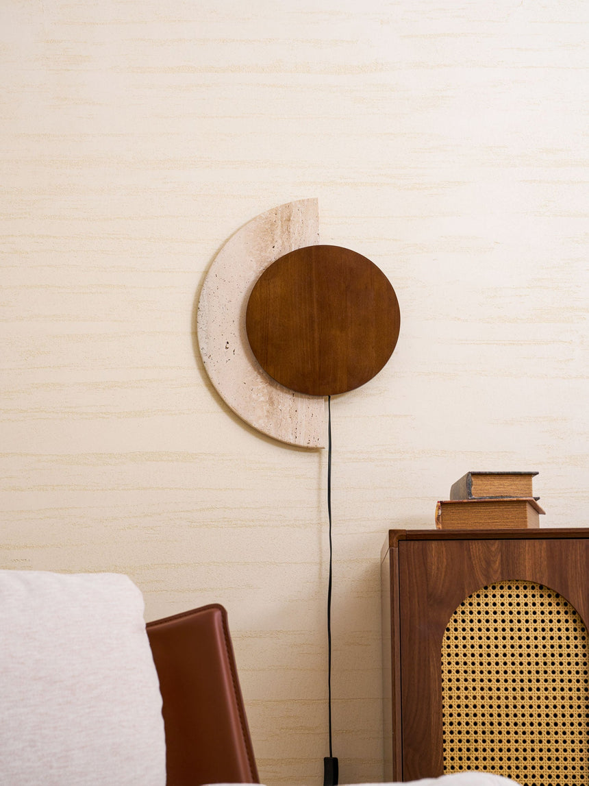 Plug in sconce lit beside a pale armchair and a cane fronted cabinet