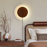 Plug in sconce lit above a nightstand beside a bed with a leather rail