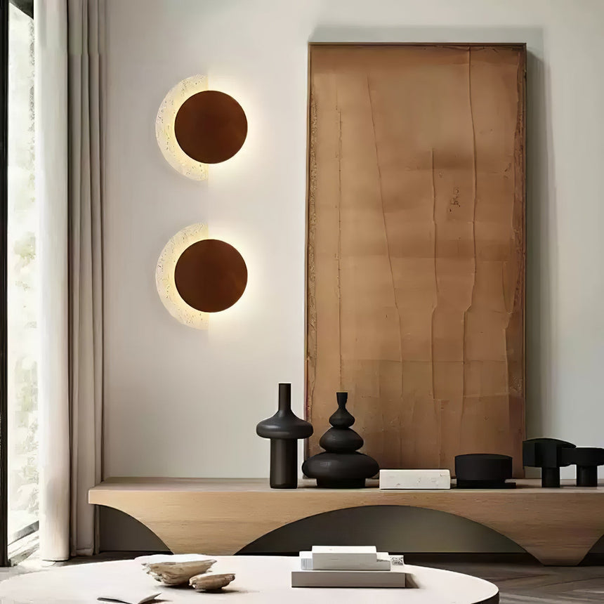 Two sconces lit on a wall beside a wood panel and a low table