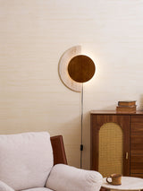 Plug in sconce lit above a sofa beside a cane cabinet and a cup