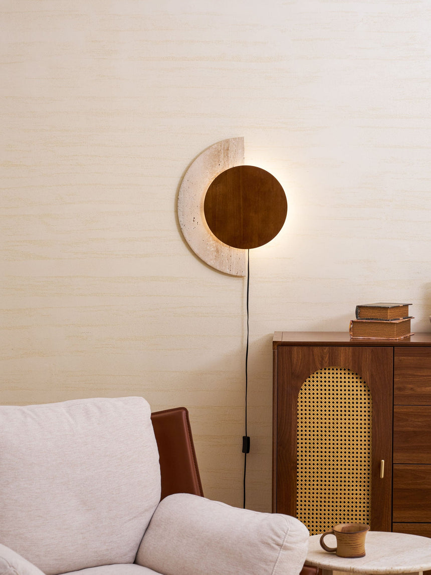 Plug in sconce lit above a sofa beside a cane cabinet and a cup