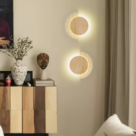 Two sconces lit on a wall above a cabinet holding vases and a bust