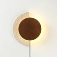 Walnut disc lit over a travertine crescent, warm halo around the edge