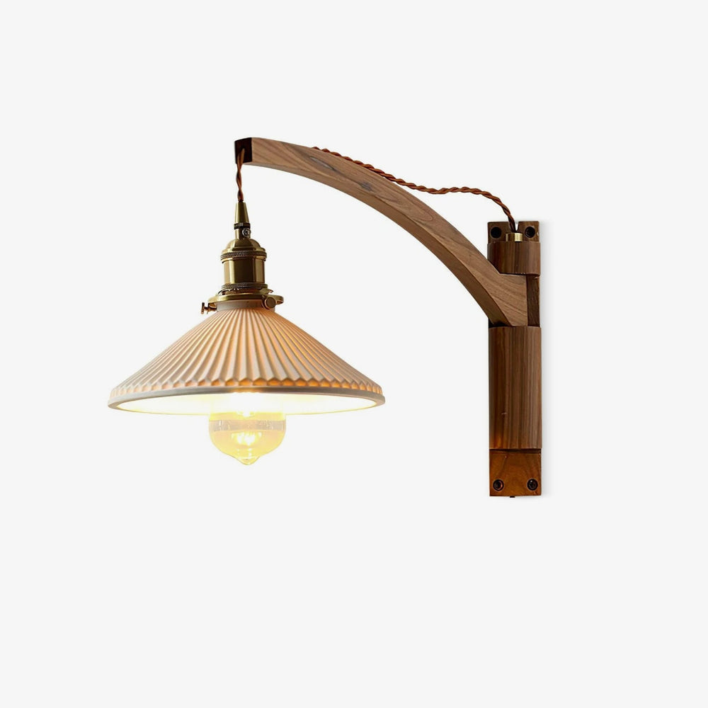 Walnut wall light with a curved wood arm and a pleated white ceramic shade on a brass socket