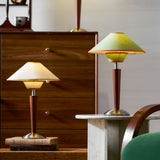 Green shade wood table lamp lit on a dark wood chest of drawers