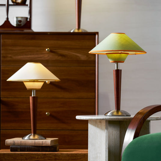 Green shade wood table lamp lit on a dark wood chest of drawers
