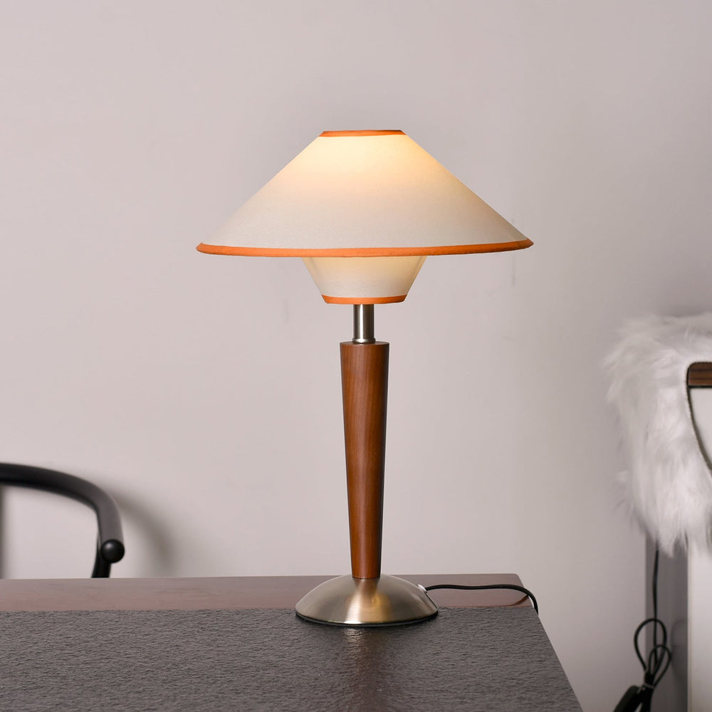 Wood table lamp with a two tier fabric shade lit beside an armchair