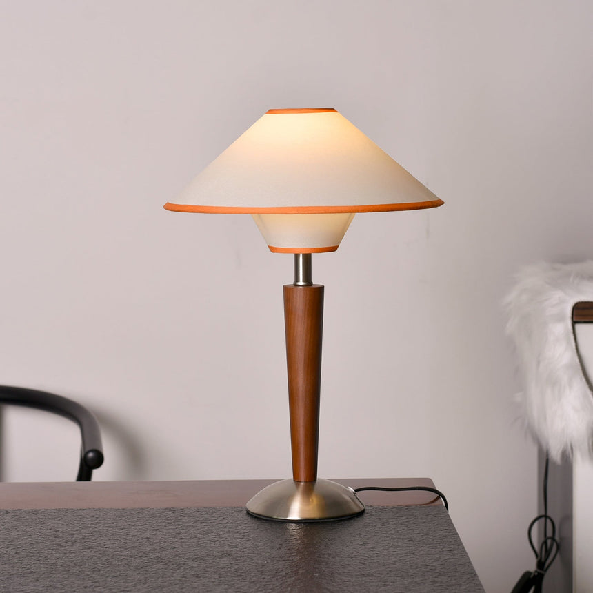 Wood table lamp with a two tier fabric shade lit beside an armchair