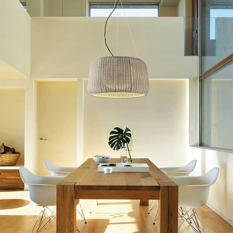The lit shade over a wood dining table with white chairs and a leaf in a vase