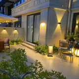 One lit in a courtyard beside planting with a lit house wall behind