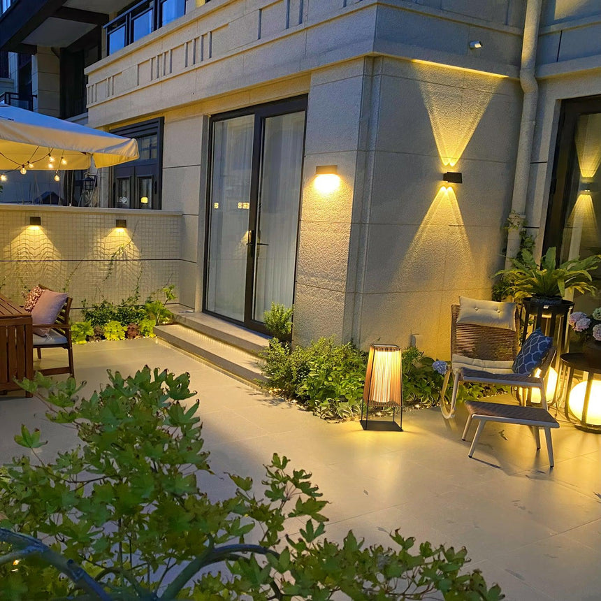 One lit in a courtyard beside planting with a lit house wall behind
